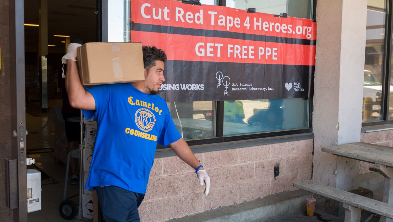 Volunteer carrying a box in front of a Cut Red Tape 4 Heroes banner